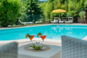 A poolside setting with two martini glasses on a woven table, a white lotus flower, and a yellow umbrella in the background. - Villa Design - Private villa, 3 bedrooms, pool, A/C, wifi, EV charger, Marche (Pergola)