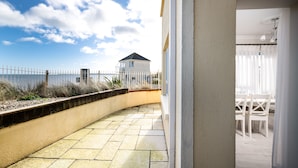 A curved patio with stone tiles, a white fence, and a building with a balcony in the background. - Seaview Apartment, Silversands, Rosslare Strand, Co. Wexford (Rosslare STrand)