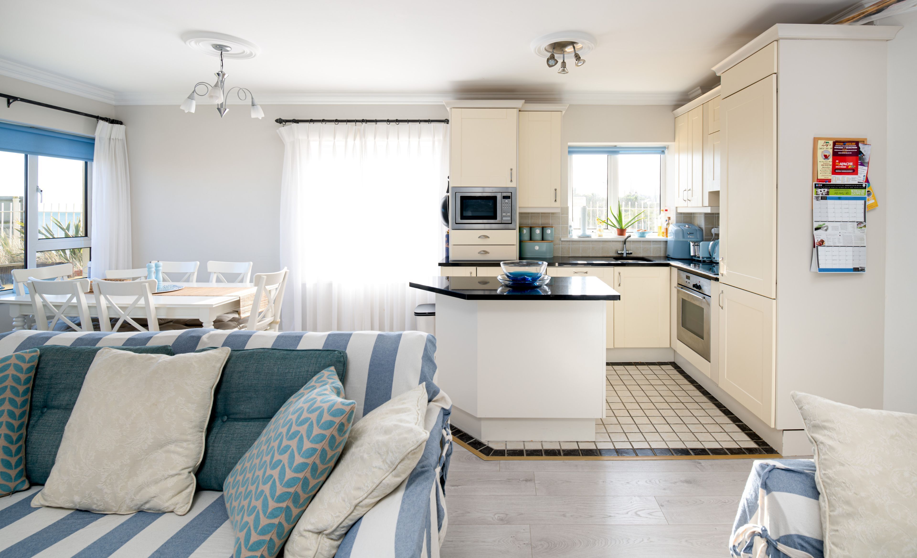 A modern kitchen with a central island, a dining area with a table and chairs, and a living area with a sofa and cushions.