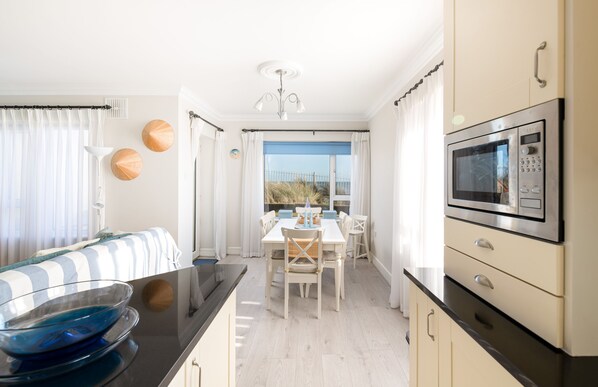 A modern kitchen with a dining area, featuring a large window, a microwave, and a bowl on the counter. - Seaview Apartment, Silversands, Rosslare Strand, Co. Wexford (Rosslare STrand)