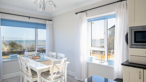 A bright room with a dining table, chairs, a TV, and a view of the beach. - Seaview Apartment, Silversands, Rosslare Strand, Co. Wexford (Rosslare STrand)