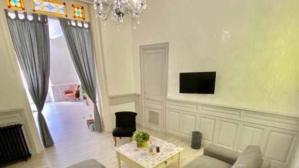 Un salon avec un canapé vert, une table basse, un lustre et un téléviseur fixé au mur.