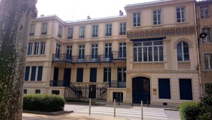 Un immeuble à plusieurs étages doté d’une cour intérieure, avec une grande entrée ornée d’une porte bleu foncé et d’un portail en fer forgé décoratif.
