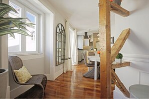 Ein modernes Wohnzimmer mit Holzboden, einem Essbereich mit weißem Tisch und einer Küche im Hintergrund.