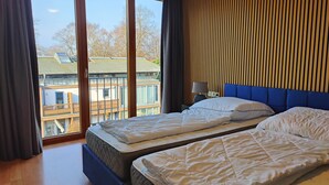 A hotel room with two beds, a large window with a view of buildings, and a wooden wall panel. - Attic apartment, Strandstr., side view. Sea view, 150 m to the Baltic Sea, renovated in 2025 (Kühlungsborn)