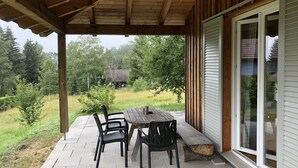An outdoor patio with a wooden table and chairs, a covered area, and a view of a house in the background.