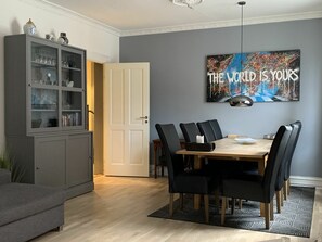 Een eethoek met een houten tafel, zwarte stoelen, een grijze kast met glazen deuren en een schilderij aan de muur.
