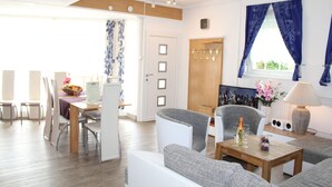 A modern living room with a dining area, a wooden door, and a window with blue curtains.