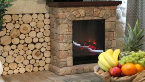 A stone fireplace with a fire, surrounded by neatly stacked logs.
