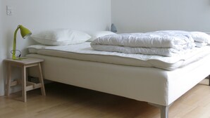 A minimalist bedroom with a wooden floor, a single bed with white bedding, and a small wooden nightstand with a green lamp.