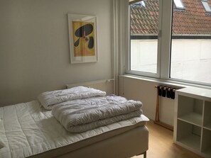 Une chambre à coucher avec un lit, un radiateur, une fenêtre et un tableau accroché au mur.