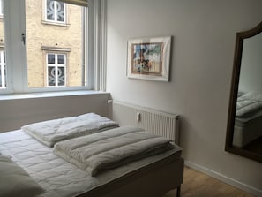 Cozy retreat with a single bed, large window, and radiator, featuring a framed artwork above.