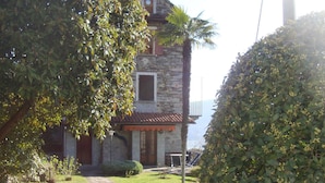 A stone house with a tiled roof, a stone pathway leading to the entrance, and a view of the sea in the background. - HOUSE OF CHARACTER LAKE MAJOR  (Oggebbio)