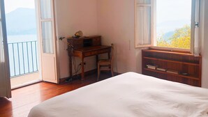 A bedroom with a bed, a desk, and a chair. There are two windows with curtains, one on each side of the bed. - HOUSE OF CHARACTER LAKE MAJOR  (Oggebbio)