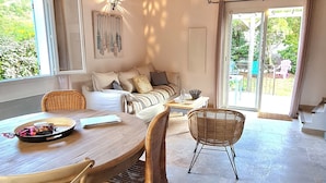A spacious living area with a high wooden ceiling, a sofa, a dining table with chairs, and a view through large sliding glass doors. - Brand new villa, fully equipped, 1.86 miles away from Palombaggia beach (Porto-Vecchio)