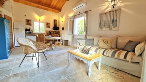 A cozy living room with a sofa, a coffee table, and wicker chairs. There's a kitchen area with a refrigerator, stove, and dining table. - Brand new villa, fully equipped, 1.86 miles away from Palombaggia beach (Porto-Vecchio)