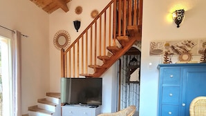 A spacious living area with a wooden staircase, a flat-screen TV, a wicker chair, and a blue cabinet. - Brand new villa, fully equipped, 1.86 miles away from Palombaggia beach (Porto-Vecchio)