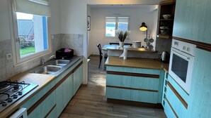 Cucina con isola centrale, piano cottura, lavello e frigorifero. Una finestra permette l'illuminazione naturale e offre vista all'esterno.