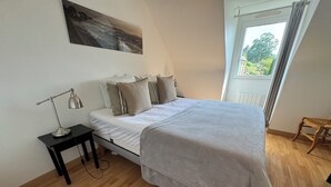 Una camera da letto con un letto, un comodino, una lampada da scrivania, una finestra con tende e un quadro appeso al muro.