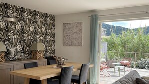 A modern kitchen with a wooden table and chairs, a decorative wall, and a view of greenery outside.