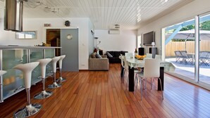 A modern kitchen with a bar area, wooden flooring, and a dining area with a table and chairs. - Cap-Ferret peninsula: Beautiful villa with heated pool (Lège-Cap-Ferret)