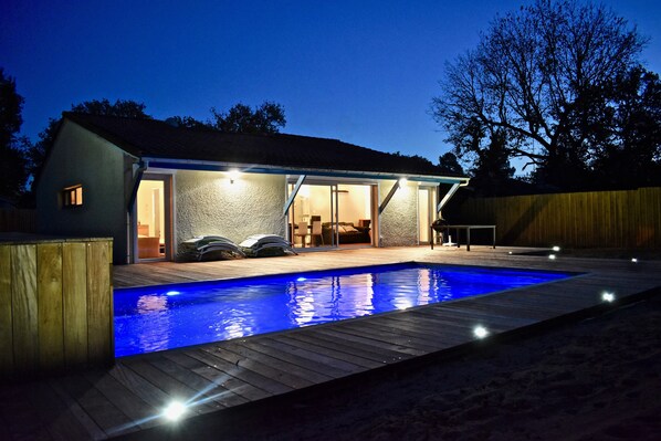 A house with a swimming pool, an outdoor patio, and a covered area with a table and chairs.