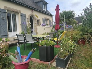 A patio area with a table and chairs, surrounded by potted plants and a red umbrella.