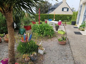 A garden with various potted plants, a palm tree, and a small outdoor seating area with a table and chairs.