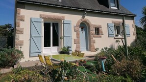 Ein zweistöckiges Haus mit Balkon, einem Essbereich mit Stühlen und einem kleinen Garten mit Pflanzen und Tisch.