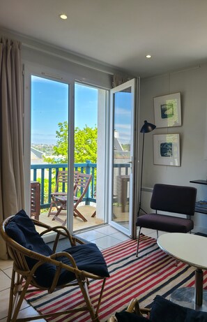 Quarto com uma grande porta de vidro deslizante que dá para uma varanda, cadeiras de vime, uma mesa redonda e um abajur.