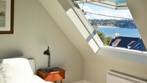 A bedroom with a skylight, a bedside table with a lamp, and a view of a coastal landscape.