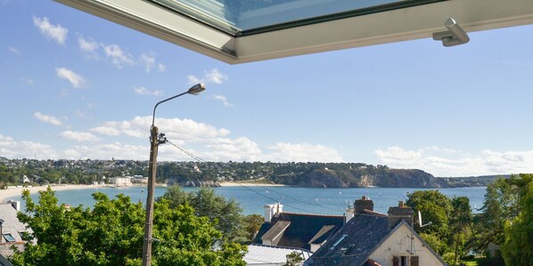 A coastal view from a window overlooking a beach, a clear sky, and a distant town. - House with Panoramic Sea View - 200 m from the beach (Crozon)