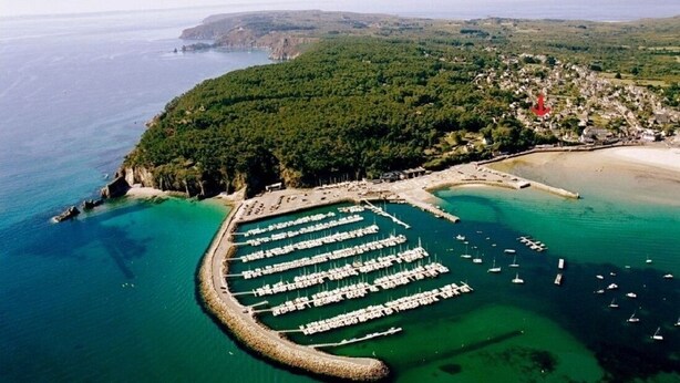 An aerial view of a coastal area with a marina, a forested peninsula, and a small town.