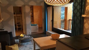 Uma sala de estar aconchegante com uma mesa de madeira, um bean bag amarelo e uma janela grande com vista para uma varanda.