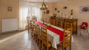A dining area with a long table, chairs, a chandelier, a radiator, and a window with curtains. - Comfortable cottage prox. Obernai between Strasbourg and Colmar wine route (Stotzheim)