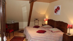 A bedroom with a bed, two pillows, a nightstand, a lamp, a chair, a desk, and a red rug. - Comfortable cottage prox. Obernai between Strasbourg and Colmar wine route (Stotzheim)