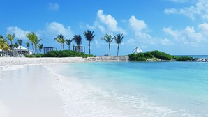 A beach with clear turquoise water, white sand, and palm trees.