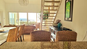 A dining area with wicker chairs and a table, a staircase, and a view of the ocean.
