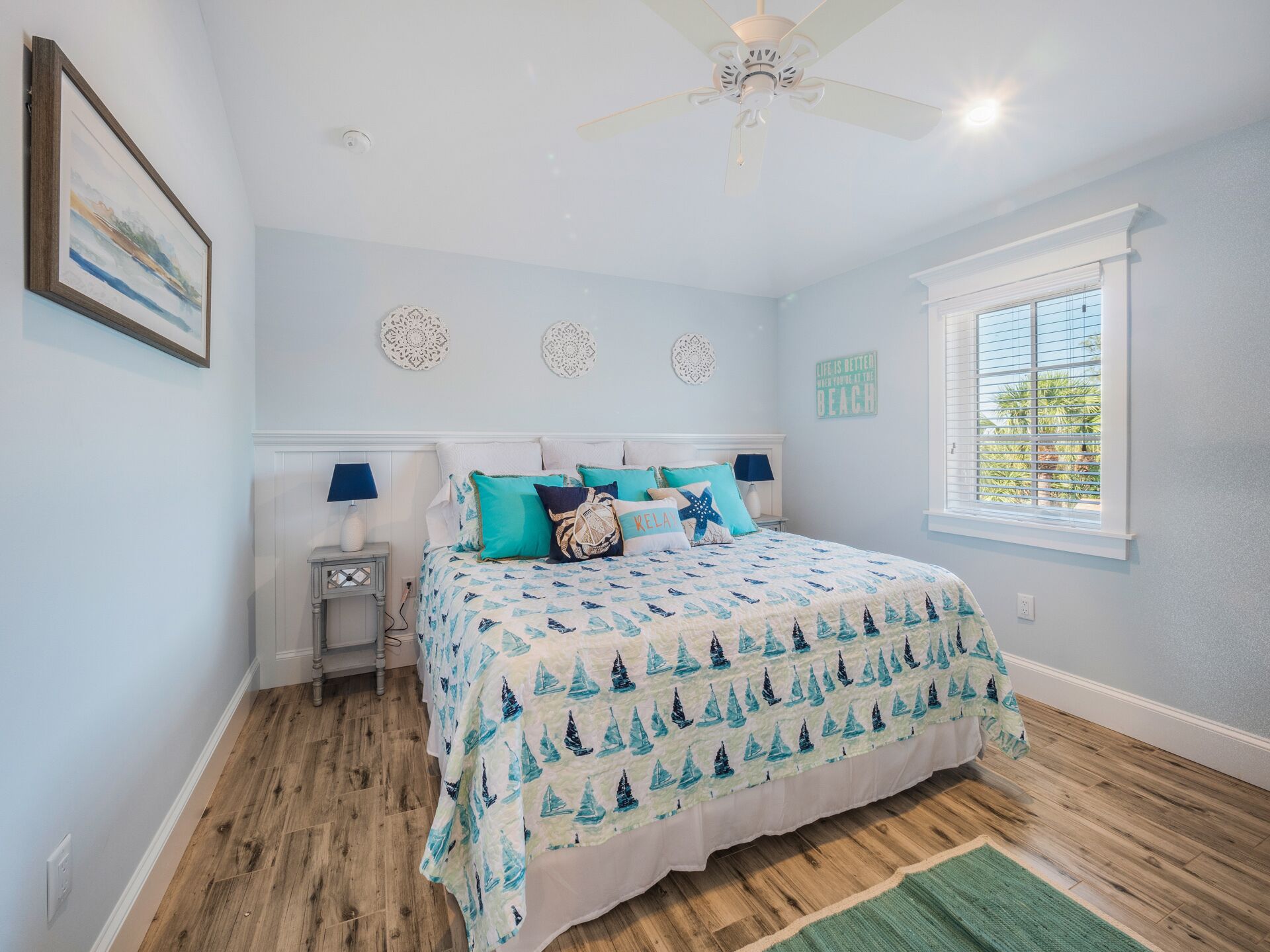 A bedroom with a bed, a ceiling fan, a window, and a wall with decorative items.