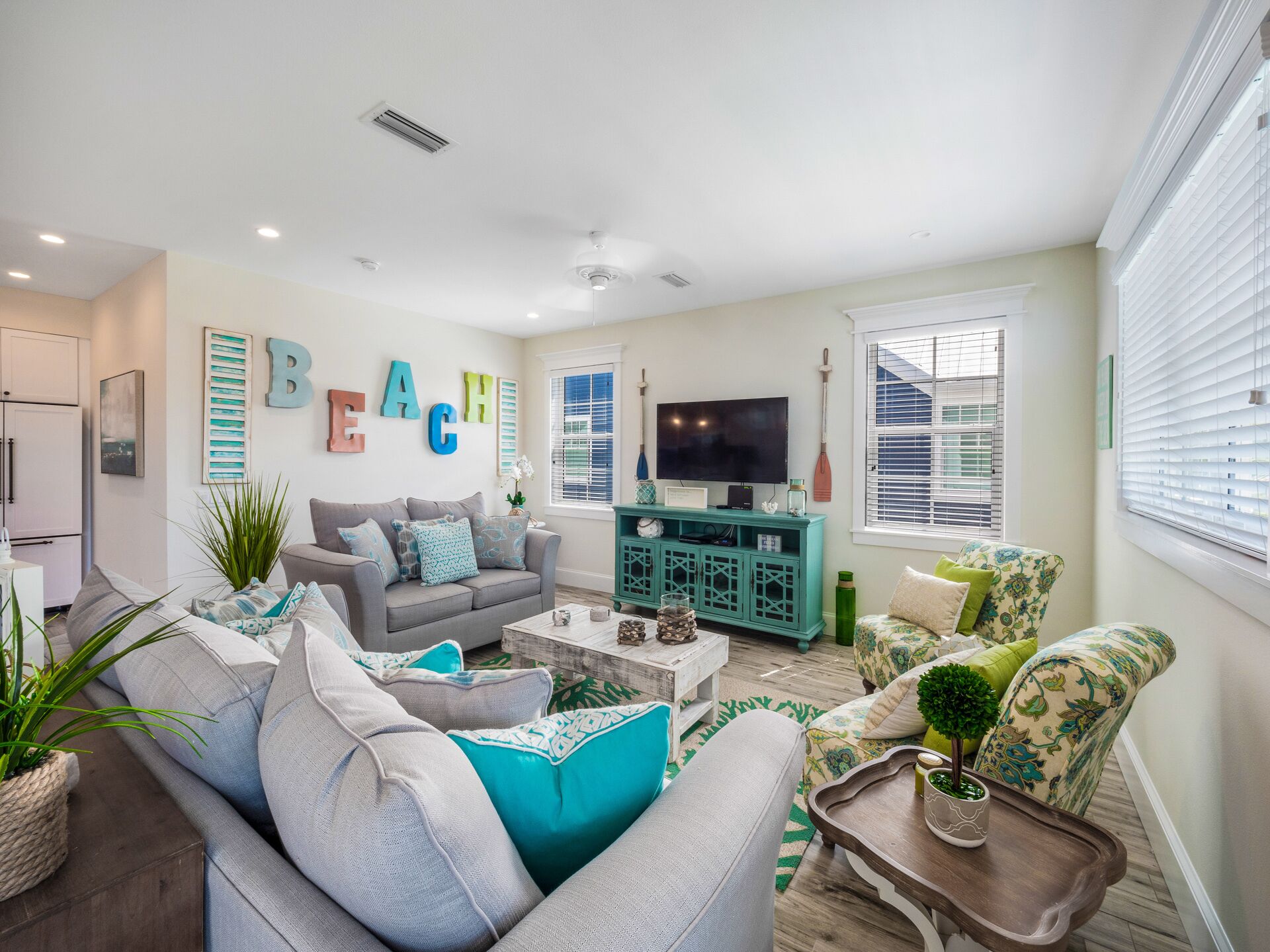 A modern living room with a grey sofa, teal accent pillows, a teal entertainment unit, and a large TV.