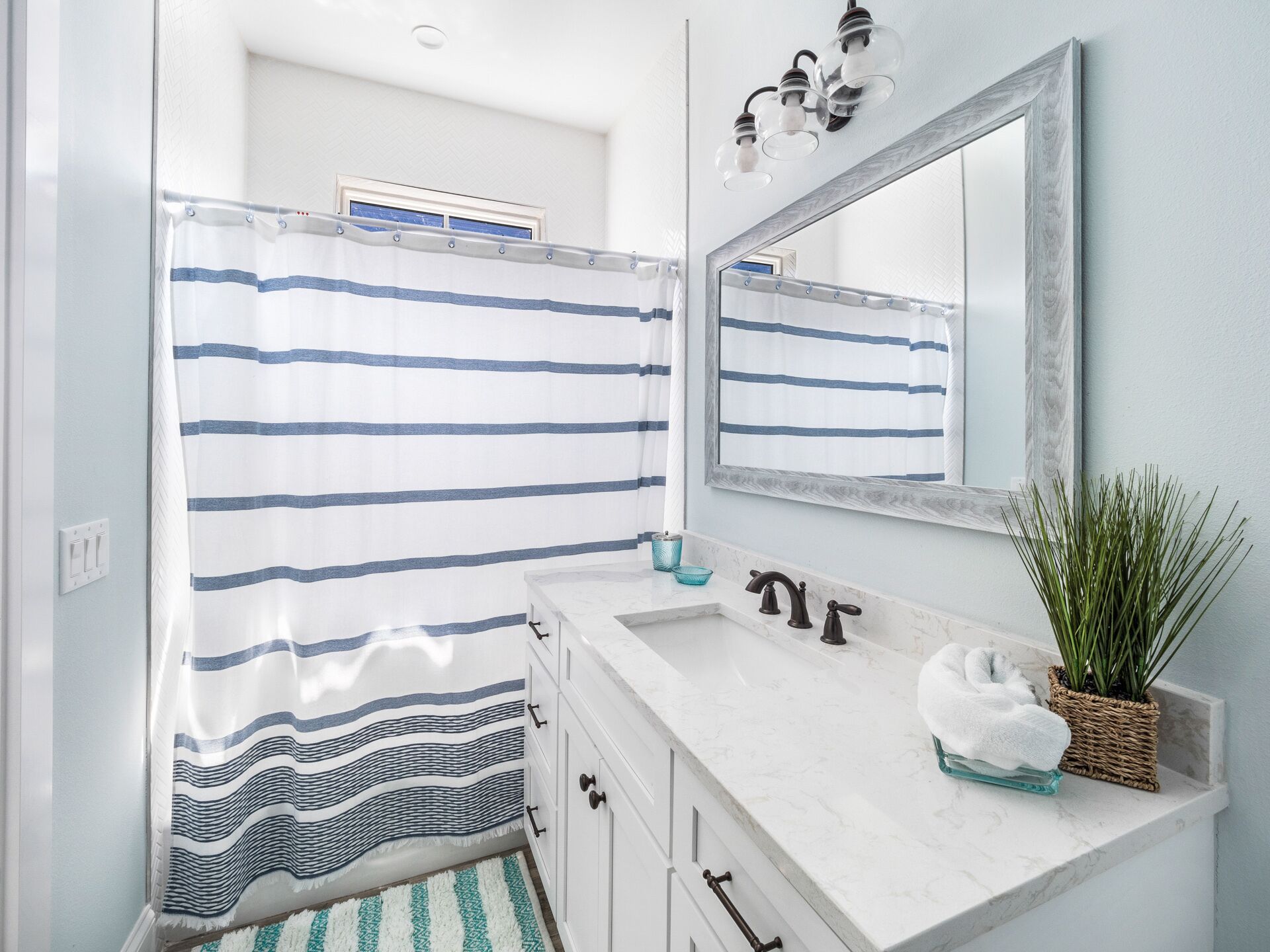 A bathroom with a striped shower curtain, a sink with a mirror above it, and a plant on the counter.