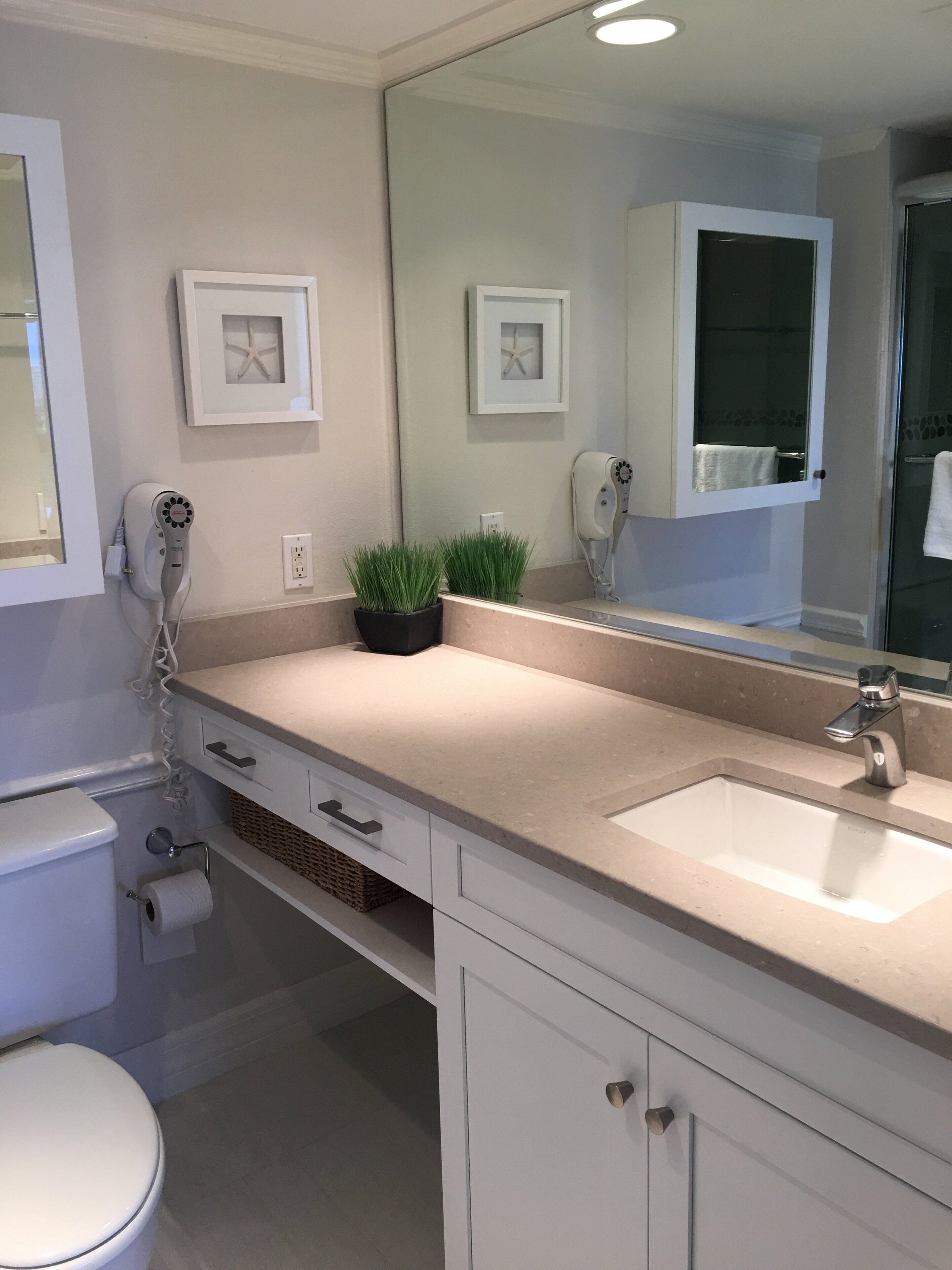 A bathroom with a toilet, a sink, a mirror, and a hairdryer on the wall.