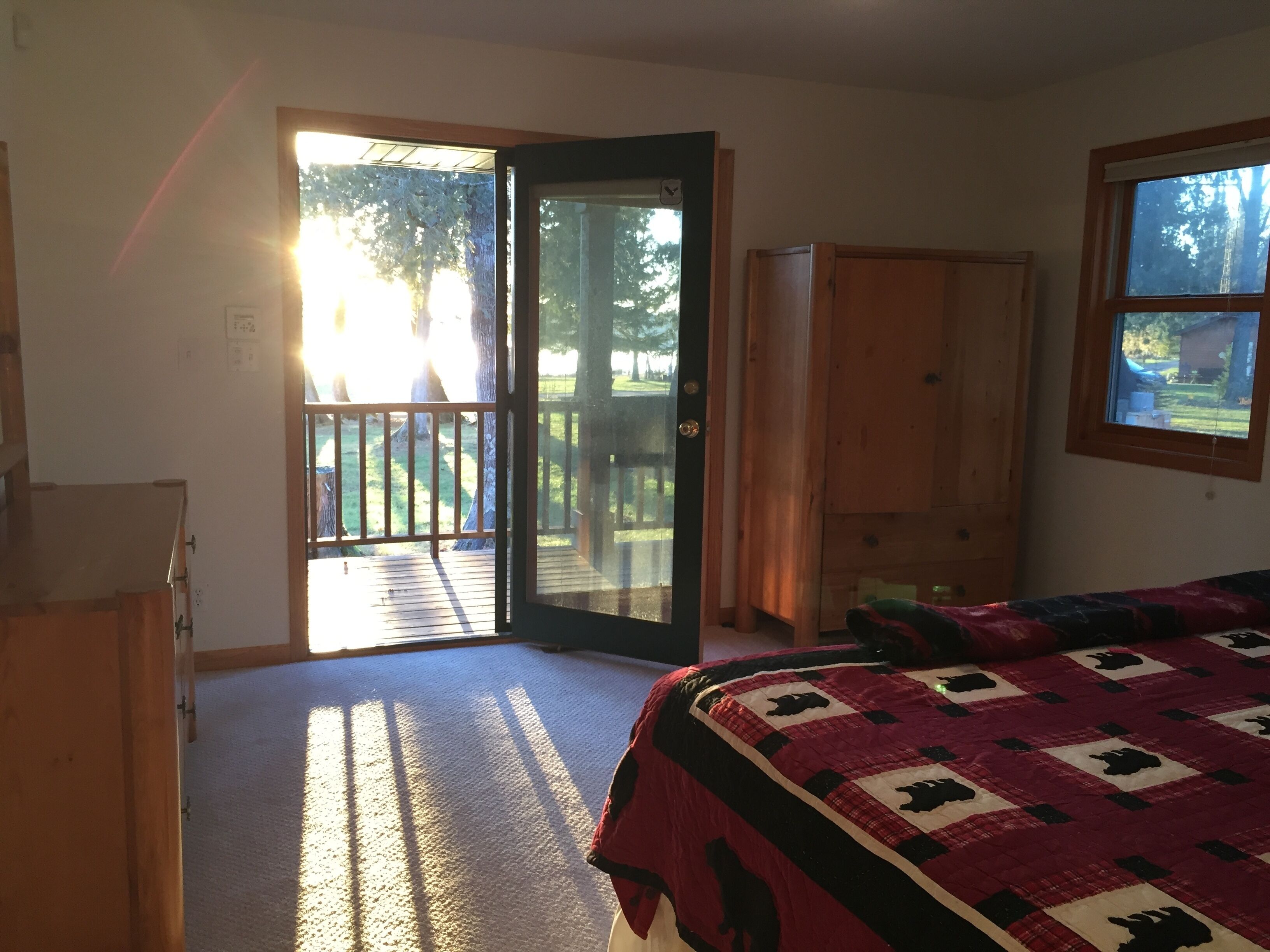 Une chambre avec un grand lit, une armoire en bois et une porte-fenêtre coulissante donnant sur une terrasse.