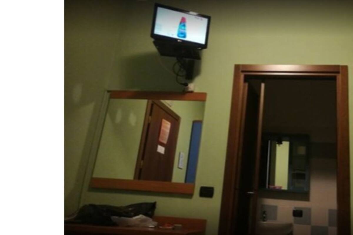 A room with a television mounted on the wall, a wooden door, and a mirror.