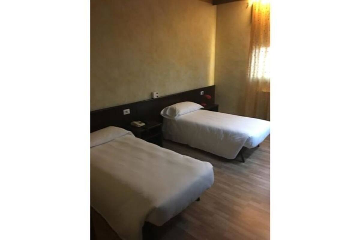 A hotel room with two single beds, a wooden floor, and a plain wall.