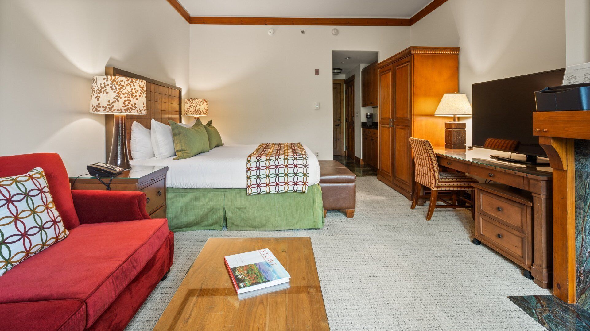 Ein Hotelzimmer mit Bett, Schreibtisch, Fernseher, rotem Sofa und Couchtisch.