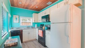 A kitchen with teal walls, white cabinets, a black oven, and a white refrigerator.