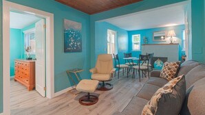 A room with teal walls, a wooden ceiling, a sofa, a chair, a dining table with chairs, and a small cabinet.