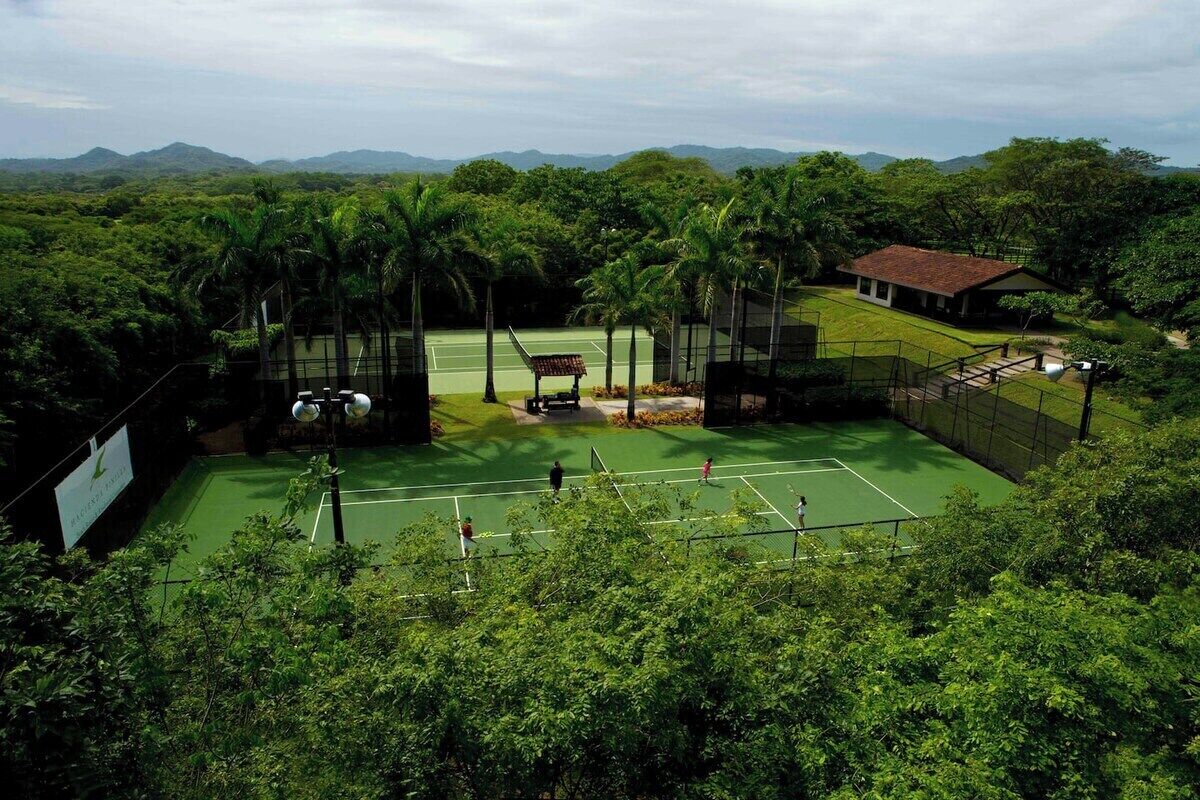 Una pista de tennis envoltada de vegetació exuberanta i amb una muntanya de fons.