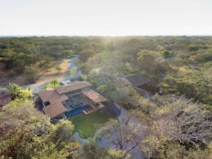 A residential property with a swimming pool, surrounded by dense vegetation and a winding road.